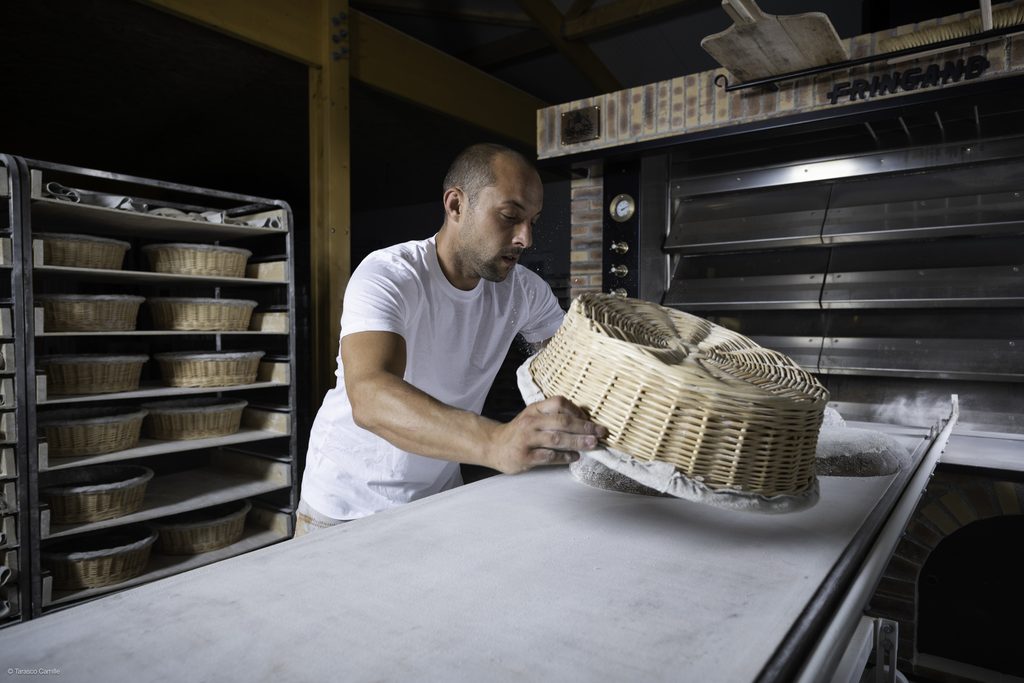 Boulanger portant une corbeille de pains devant son four